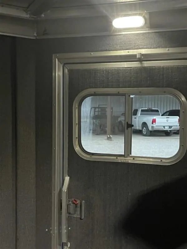 1999 Elite Custom 3 Horse Trailer – Rotating Saddle Rack – Interior view of the tack room door window looking out toward trucks