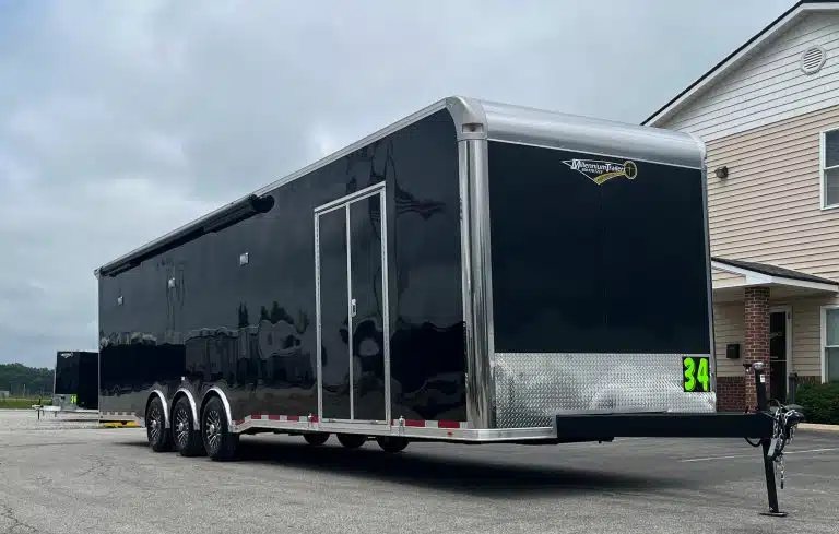 2025 Millennium 34 ft Car Trailer – Corner Bathroom – Three-quarter front view of a black enclosed trailer with triple axles and hitch