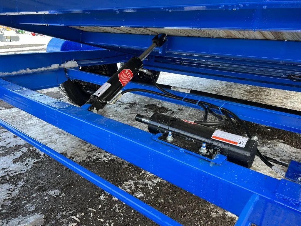 2024 Rice Trailers 20 ft Tilt Trailer – Spare Mount – Under-deck view of the hydraulic tilt cylinders and blue metal trailer frame