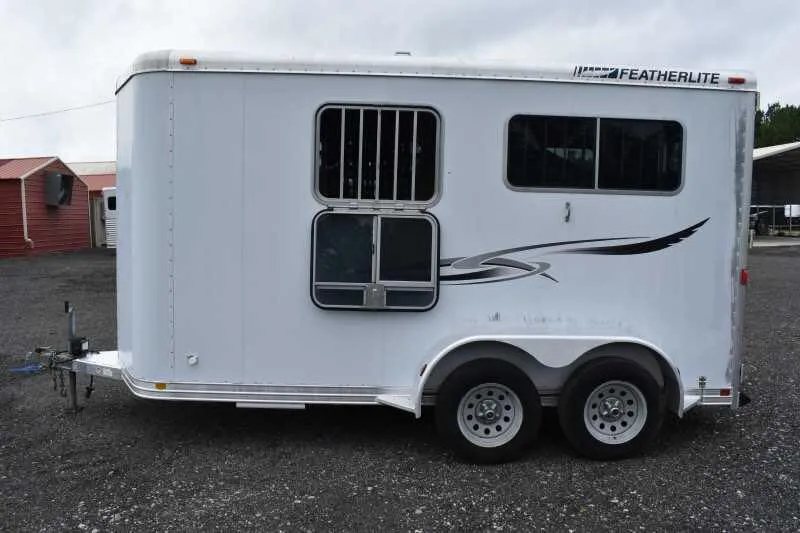 2003 Featherlite 2HST 2 Horse Trailer – Aluminum – Side profile view showing graphics and dual axles on the gravel ground