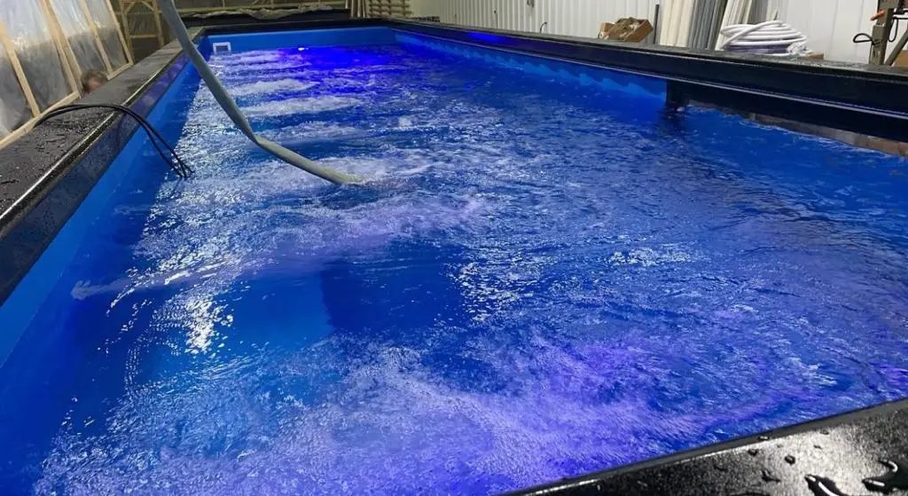 40ft Custom Container Pool – Side Viewing Window – illuminated pool water with hoses inside a workshop