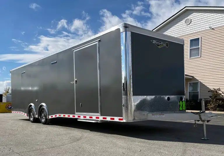 2026 Millennium 28 ft Aluminum Car Hauler – Extreme – A front three-quarter view of a dark grey enclosed trailer outdoors under a blue sky