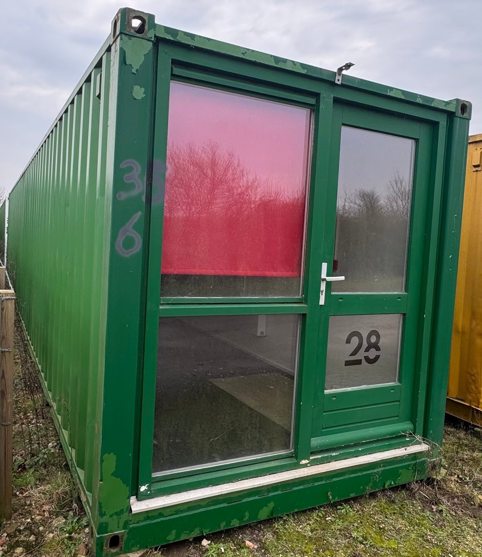 40ft Container Home – Two-Room Conversion – A green 40 foot converted container home featuring a large glass entry door and windows for natural light