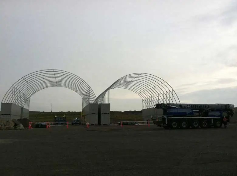 Container Shelter – Domed Tensile Membrane Cover – Two large metal shelter frames being assembled in an open field area