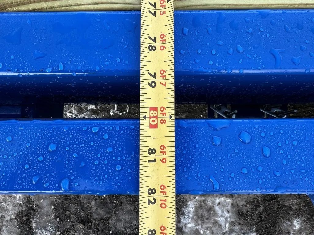 2024 Rice Trailers 20 ft Tilt Trailer – Spare Mount – A yellow measuring tape held against the blue metal frame of the trailer