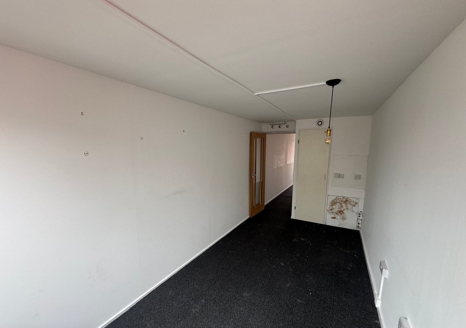 40ft Container Home – Two-Room Conversion – The interior layout of a 40 foot converted container home featuring dark carpeting and basic electrical fixtures