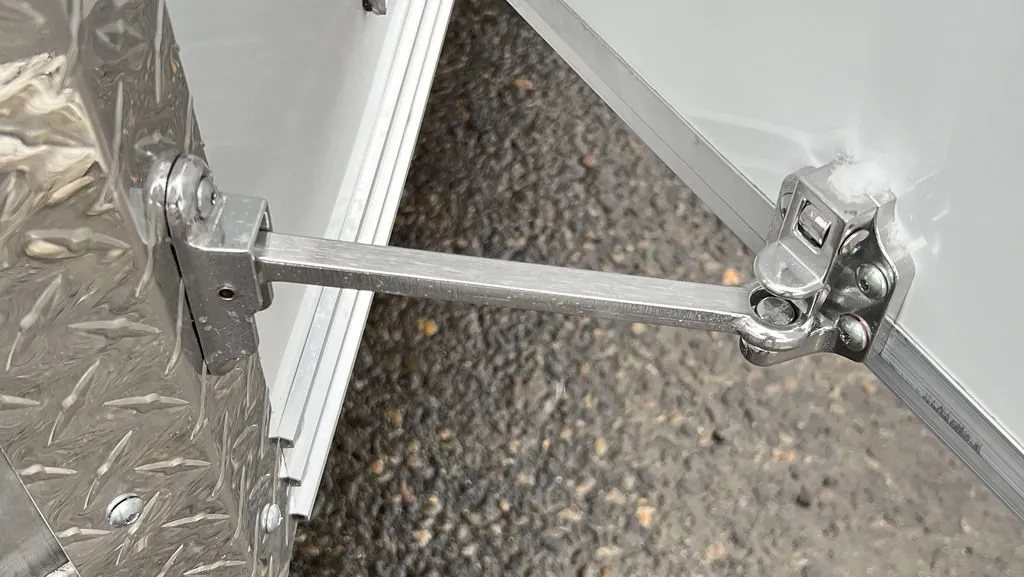 2024 E-Z Hauler 24 ft Trailer – Rear Canopy – Detail of a metal door holder arm attached to the trailer's diamond plate