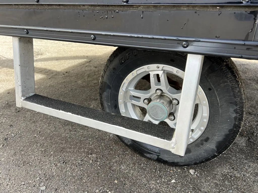 2021 Mission Trailers 2-Place Hybrid – Blackout Package – Close-up of the trailer step and tire assembly against the black side