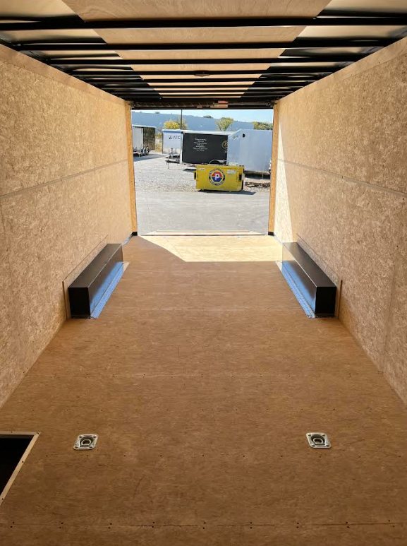 2026 Millennium 24 ft Car Hauler – Charcoal Hero – Interior view facing the rear ramp opening with plywood walls and tie downs