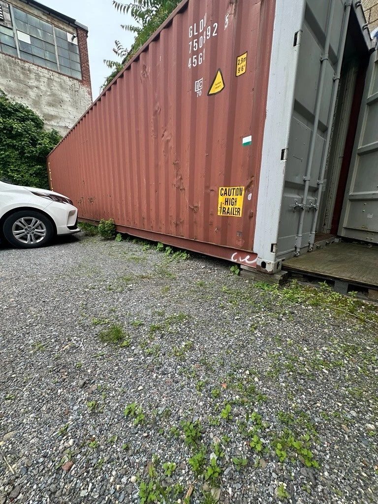 40ft High Cube Shipping Container – Used, Double Rear Doors – weathered shipping container with partially open doors beside parked car