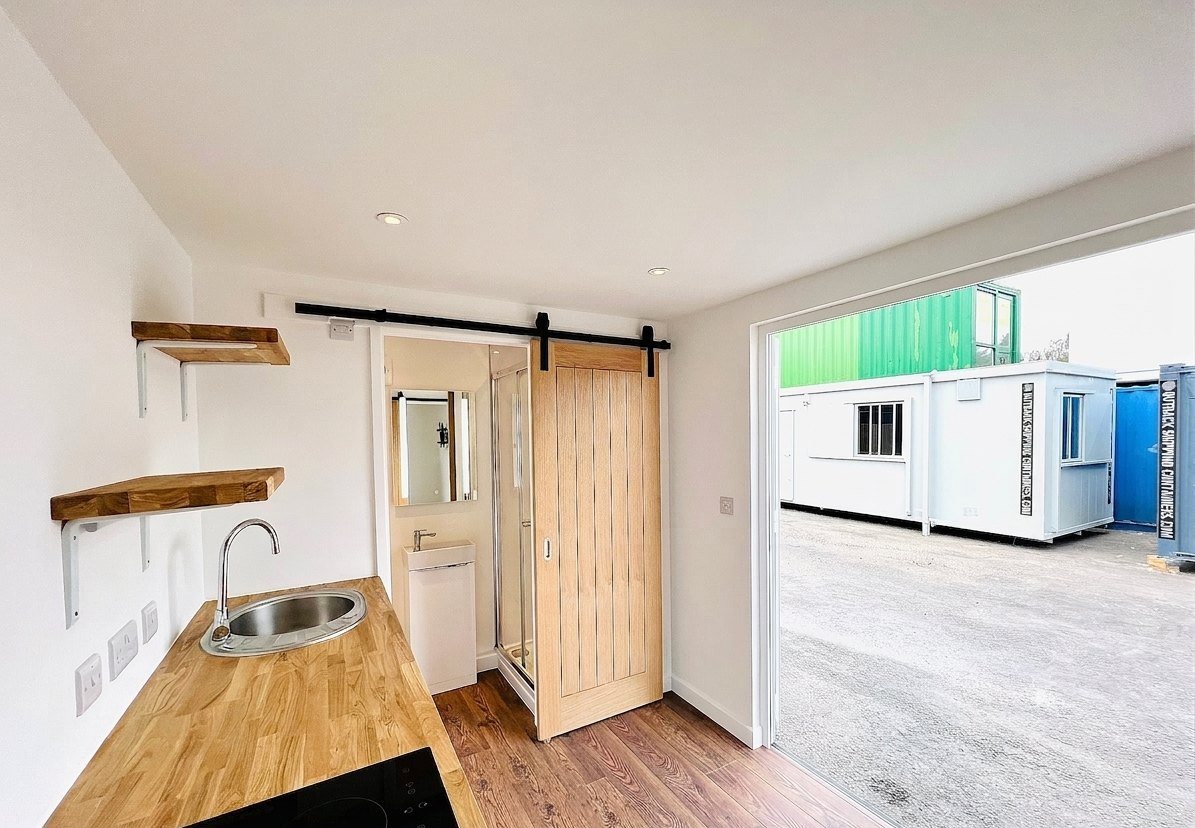 20ft Container Home – One Bed Box, 1 Bedroom – The compact interior features a fully functional kitchenette with oak surfaces and a sliding door leading to the ensuite bathroom