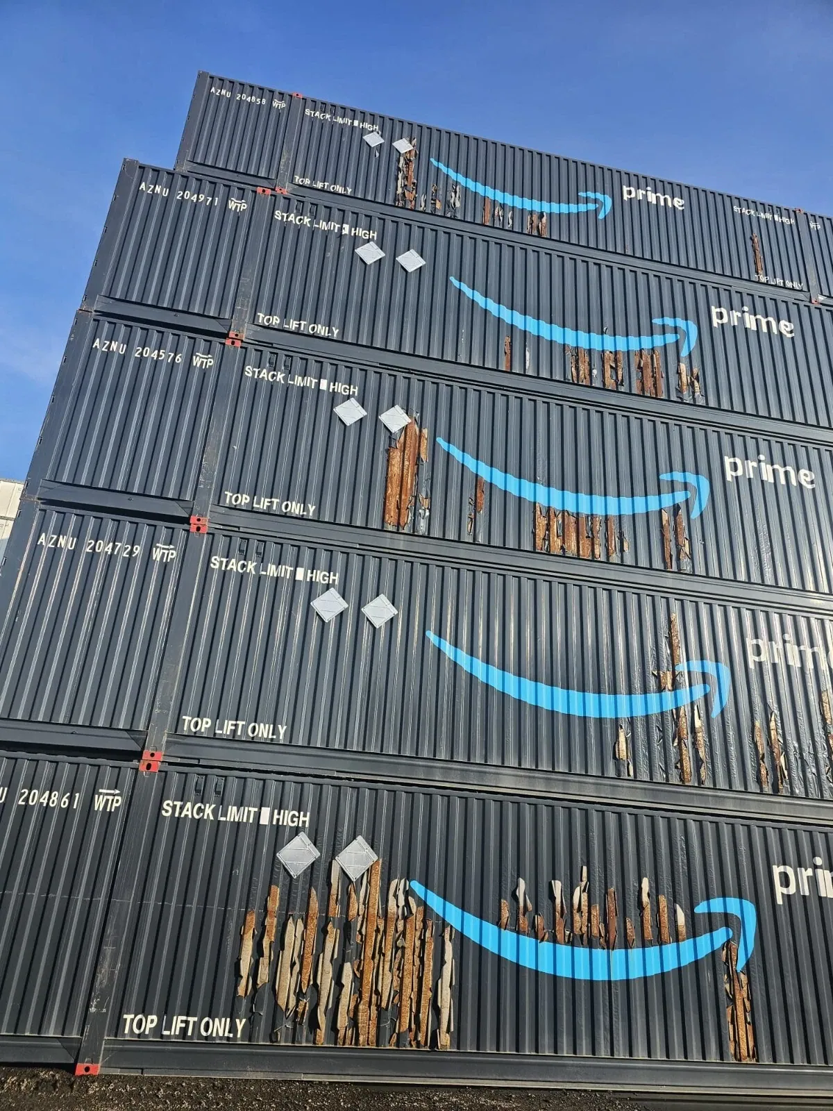 53ft High Cube Shipping Container – Used, Multi-Trip – stacked dark containers with extensive peeling paint and rust