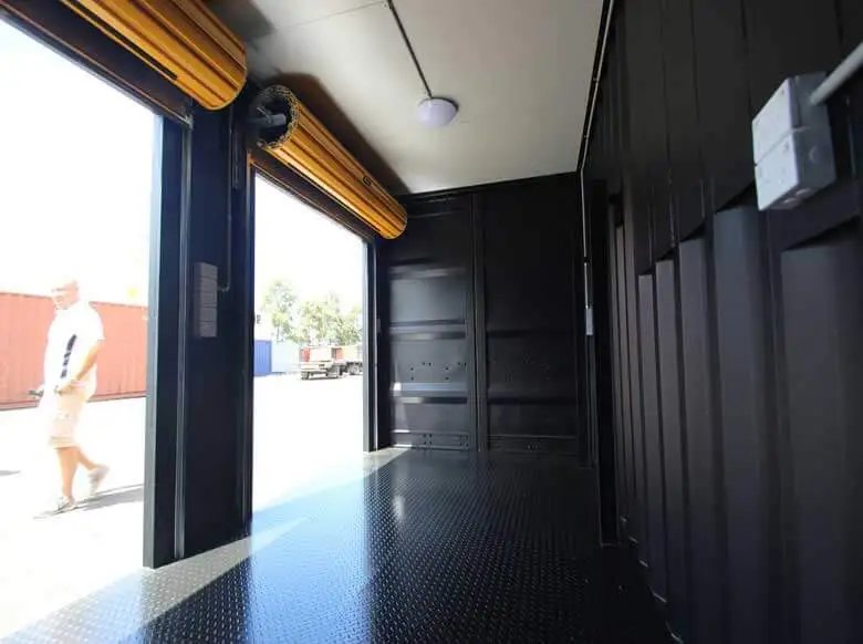 Trade Show Display Container – Lockable Steel Booth – Interior view of a black container with open roller doors and diamond plate flooring