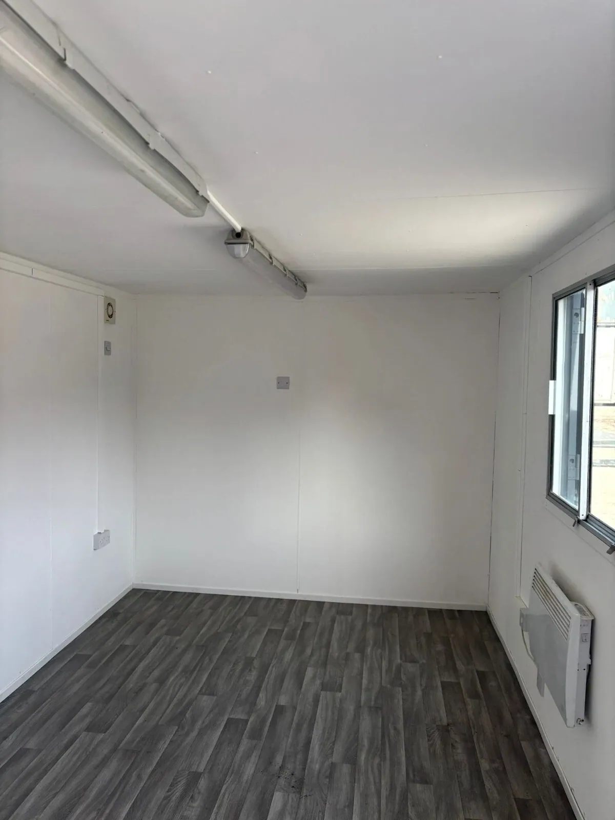 20ft Office & Canteen Container – Partitioned Storage – Empty office interior with wood-effect flooring, window and wall heater