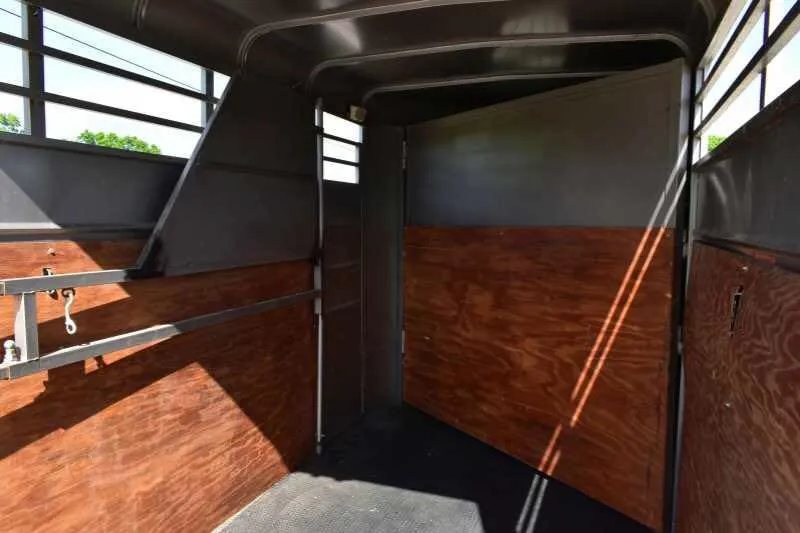2010 Calico 2 Horse Trailer – Steel, Walk-In Dressing Room – Interior horse stall area with wood-lined walls and rubber floor mats