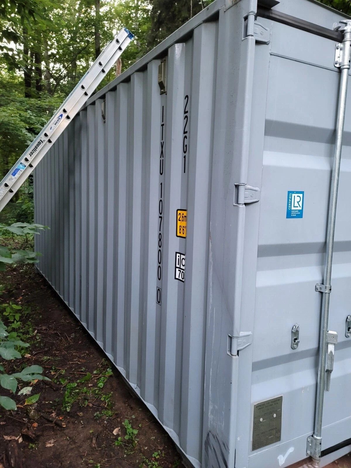 20ft Used Shipping Container – Wind & Watertight Storage – Grey shipping container side and closed door with a ladder leaning against it