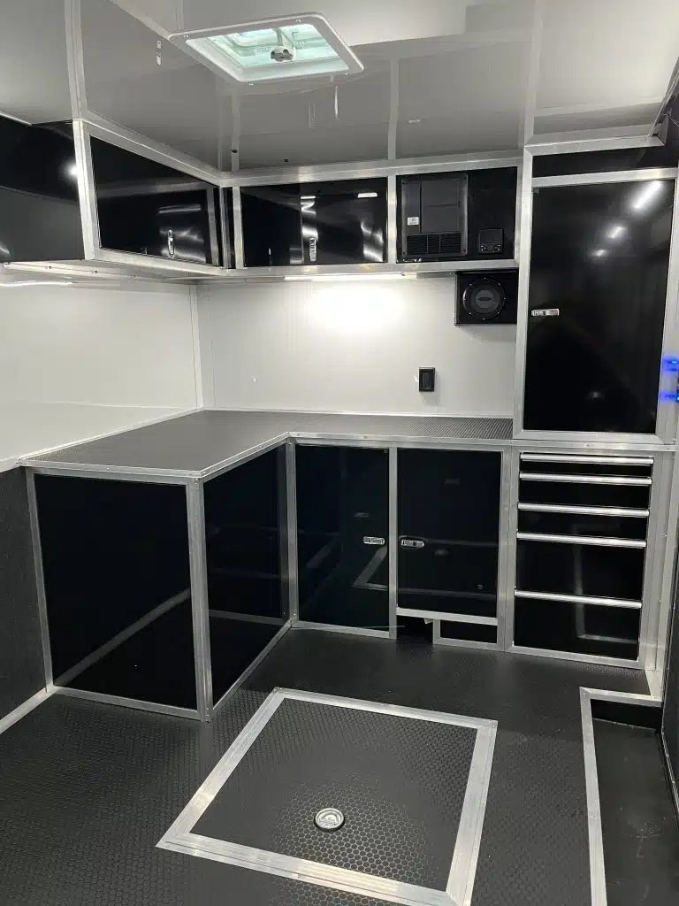 2025 Haulmark Edge 28 ft Car Trailer – Blackout, Turbo – Close up of interior black cabinets and storage bench in front of trailer