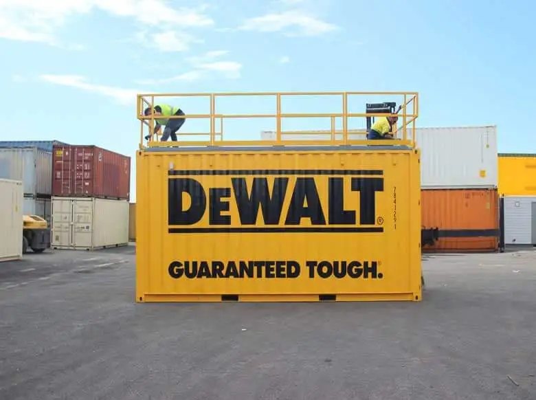 Trade Show Display Container – Lockable Steel Booth – Full side view of the yellow container with large black text and roof railing