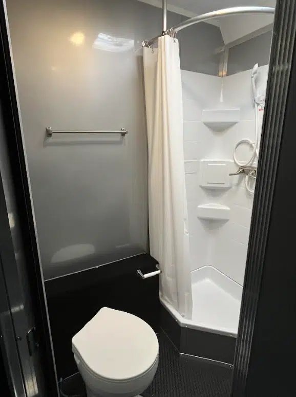2025 Millennium 34 ft Car Trailer – Corner Bathroom – Corner bathroom interior featuring a white toilet and a shower with a curtain