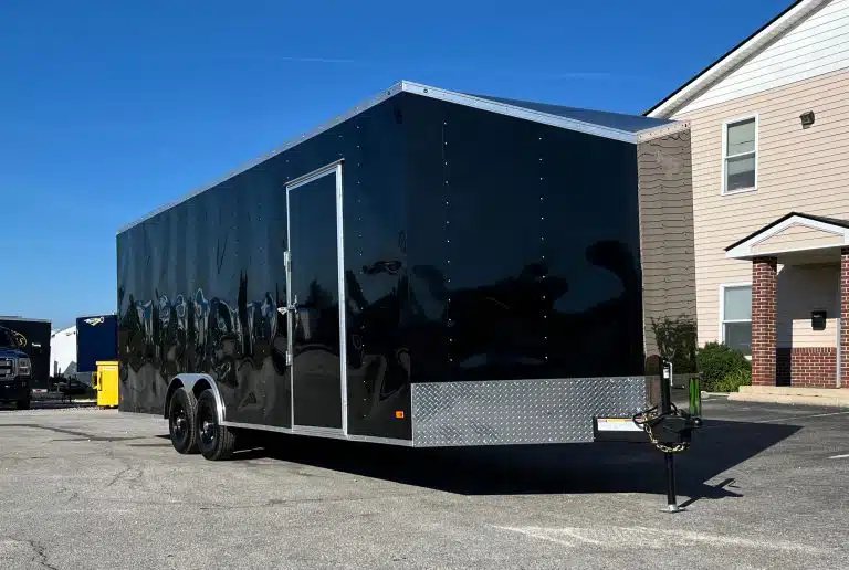2026 Millennium 24 ft Car Hauler – Black Hero – A black enclosed trailer showing the curb side with a side entry door and tandem axles