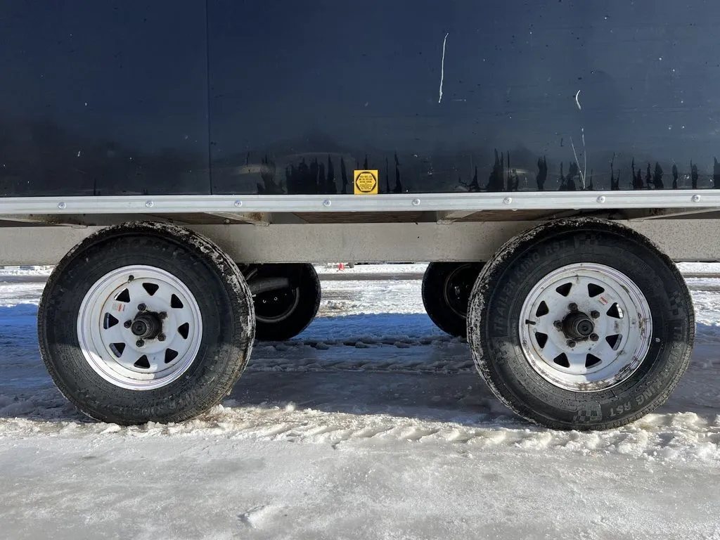 2008 Sno Pro 4-Place Snowmobile Trailer – Black Aluminum – Close-up of the tandem wheels and axles on a snowy surface