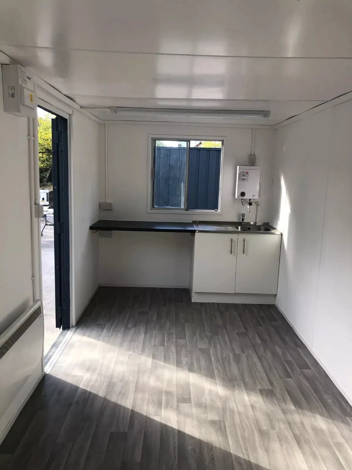 20ft Refurbished Office Container – Kitchenette & Security Shutters – compact kitchenette with sink, white cabinet and grey flooring