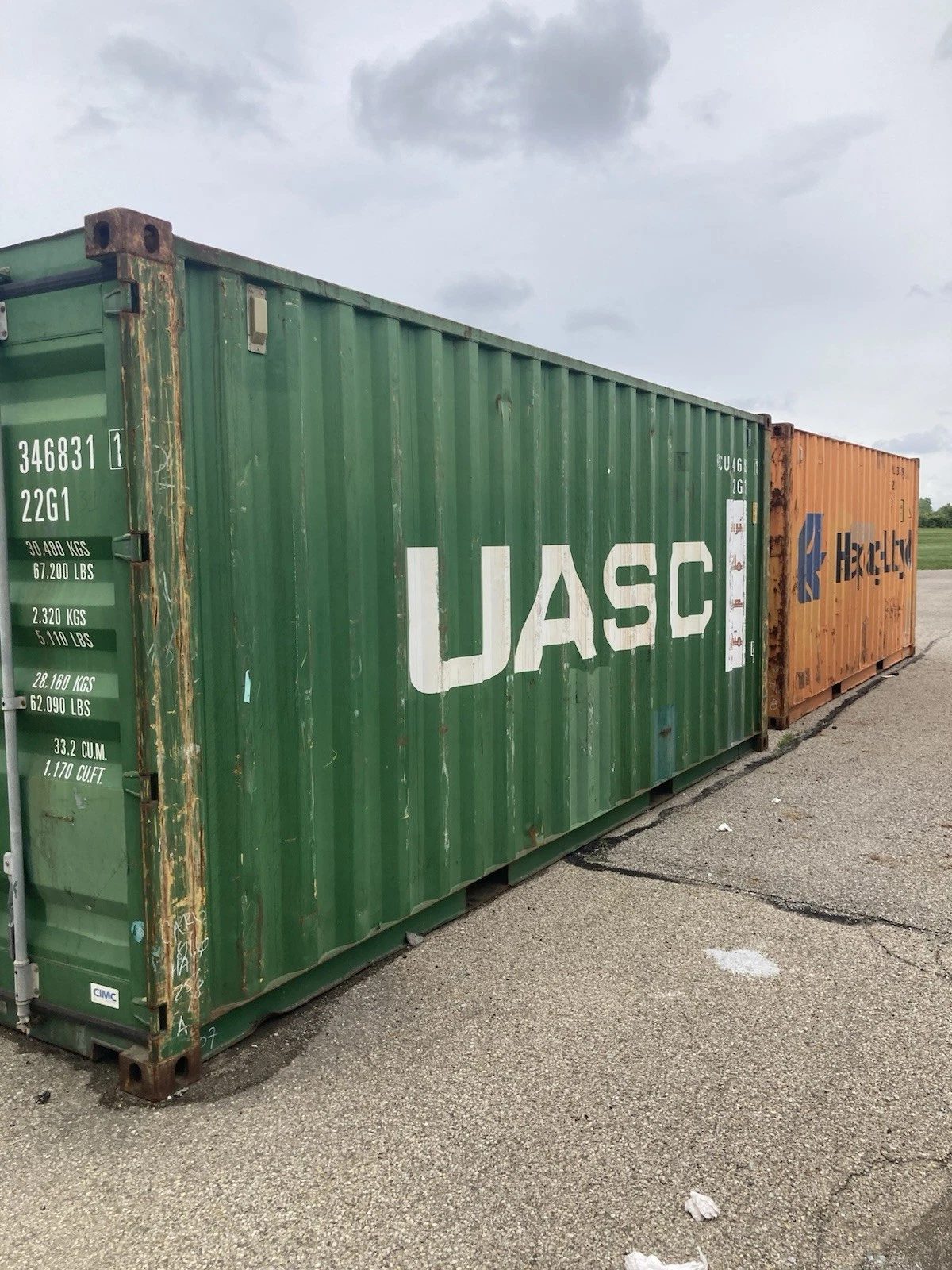 20ft Used Shipping Container – Ground-Level Storage – weathered green shipping container with orange container behind