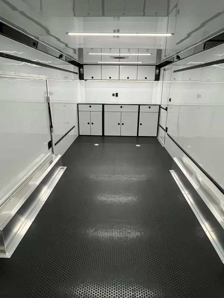 2025 ATC 24 ft Car Hauler – Large Escape Door – Interior front view showing white cabinets and black textured floor with recessed lighting