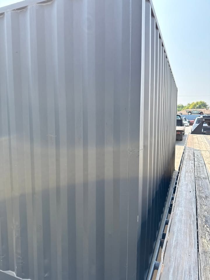 20ft Used Shipping Container – Matte Black, Side Roll-Up Door – cropped container corner and corrugated walls beside flatbed trailer