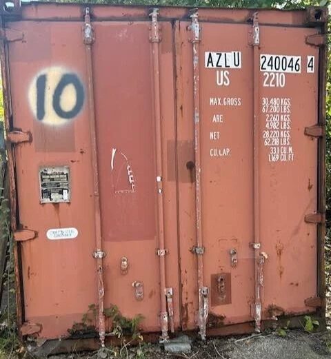 20ft Used Shipping Container – Double Cargo Doors – closed cargo doors with rust and surrounding vegetation