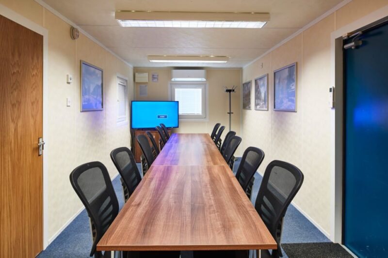32 ft ECOlink Meeting Room Cabin – Blue – Interior meeting room view with long wooden table, black mesh chairs, and wall-mounted monitor