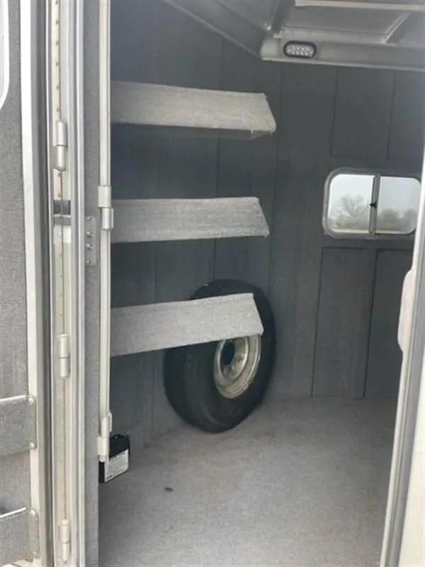 1999 Elite Custom 3 Horse Trailer – Rotating Saddle Rack – Tack room corner showing a spare tire and carpeted saddle racks