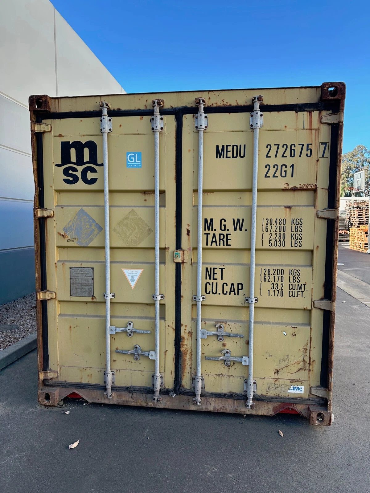 20ft Used Shipping Container – Yellow/Gold, Double Cargo Doors – Closed yellow container doors with locking bars, rust patches and identification markings