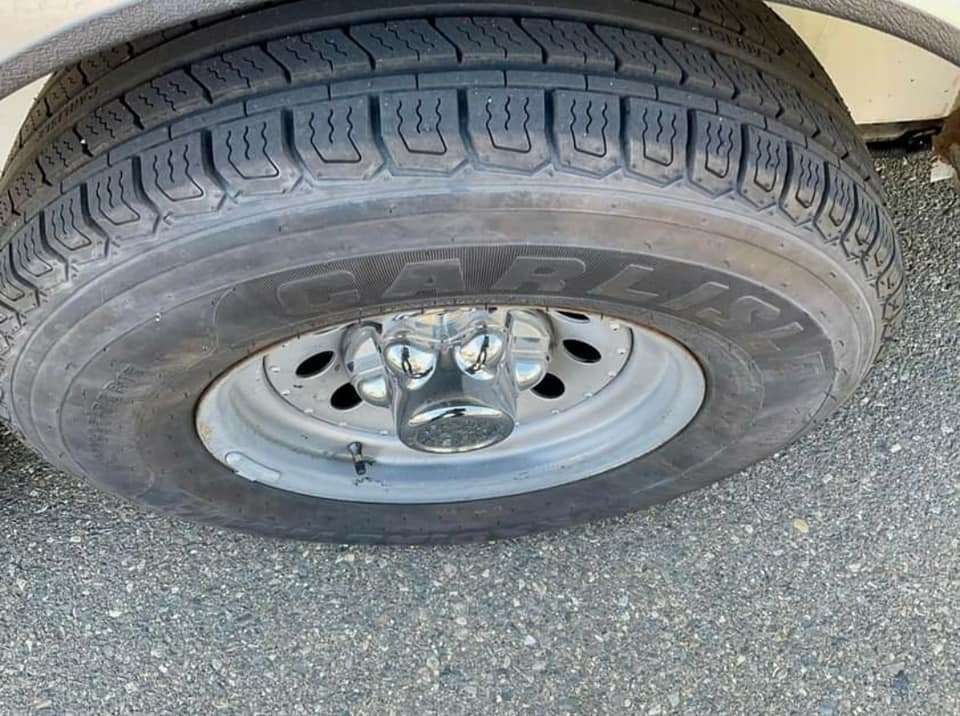 1999 Sundowner 3 Horse Trailer – Removable Rear Tack – Close-up of a trailer tire and chrome-finished wheel assembly on pavement