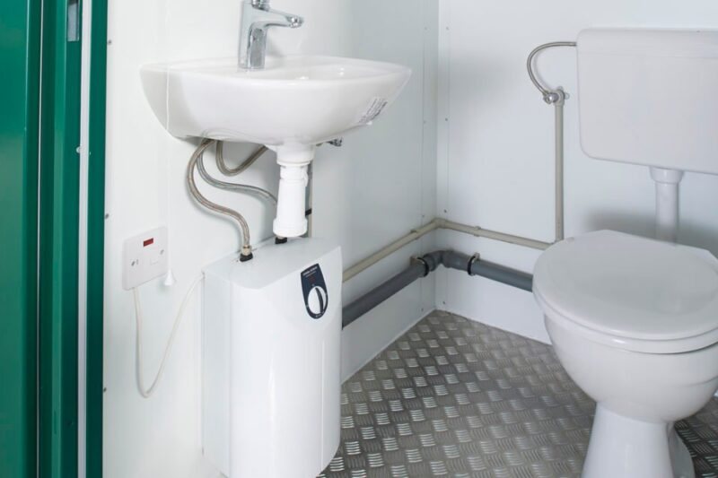 Double Mains Toilet – Green, Two Toilets – Interior view showing a sink with water heater and a toilet