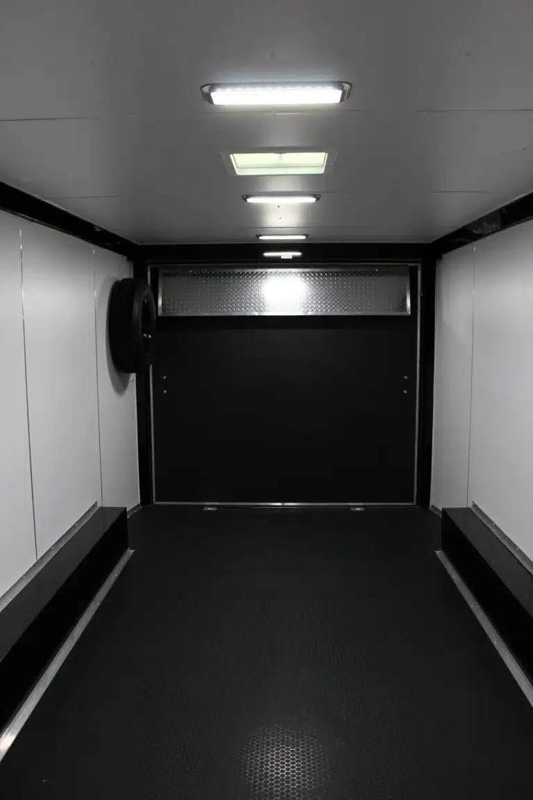 2025 Millennium Blaze 20 ft Enclosed Car Hauler – White – Finished interior of car hauler with white walls, black floor, and ceiling lights