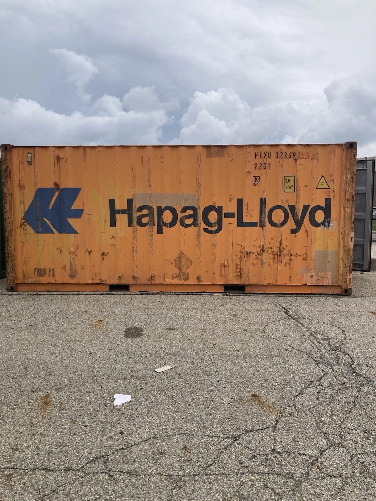 20ft Used Shipping Container – Ground-Level Storage – Side view of weathered orange shipping container on pavement