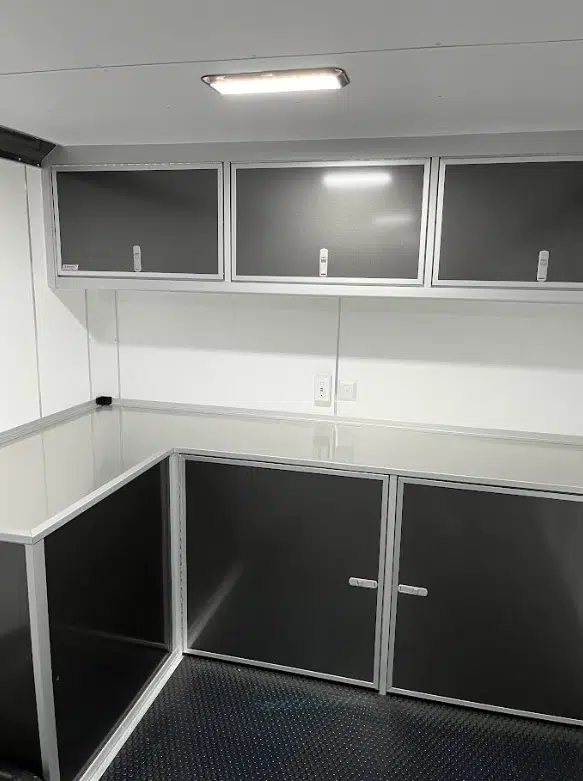 2026 Millennium 28 ft Aluminum Car Hauler – Extreme – Close-up view of the interior L-shaped workbench and upper storage cabinets in charcoal grey