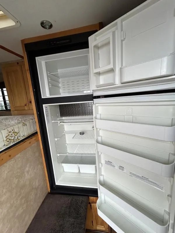 2002 Silverado 3 Horse Gooseneck Trailer – Wood Interior – Open refrigerator door inside the trailer living quarters showing shelving