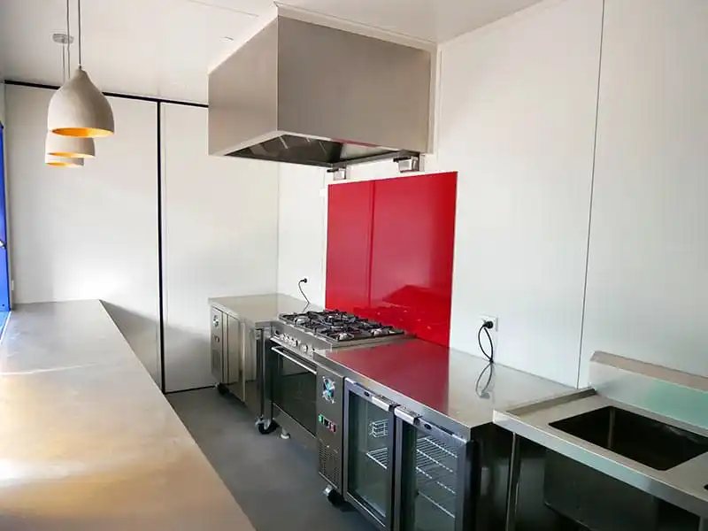 Shipping Container Kitchen – Insulated, Lockable – Industrial kitchen space with stainless steel counters, stove, and red backsplash