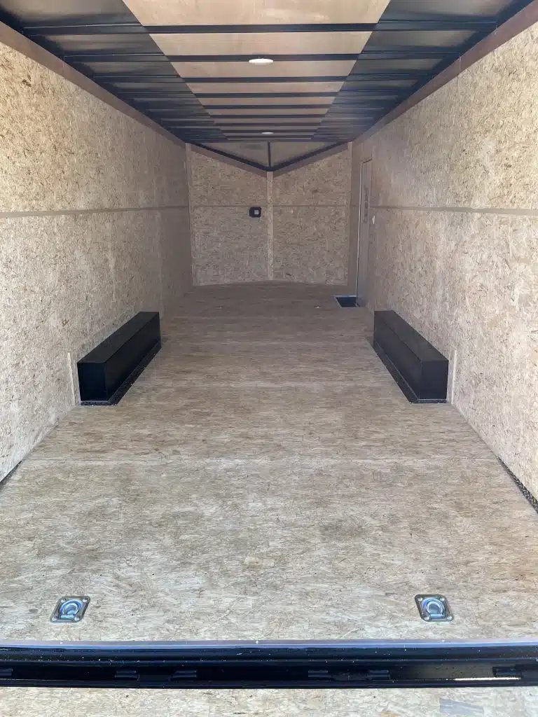 2026 Millennium 24 ft Car Hauler – Black Hero – Interior view of the empty trailer with wood walls, floor, and black wheel wells