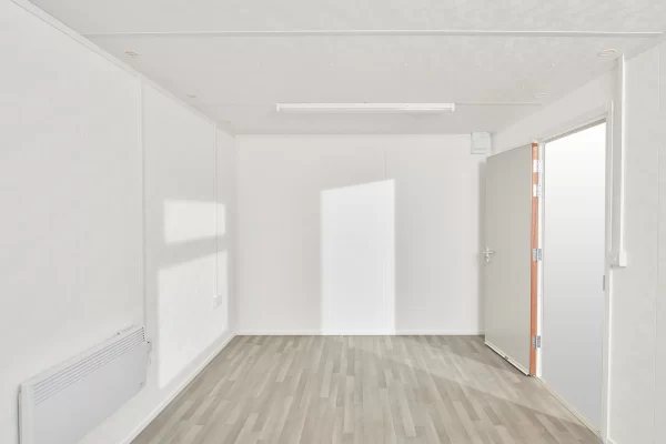 16 ft Jackleg Office Cabin – Open Plan – Empty interior of a white site office showing wood-effect flooring and a heater