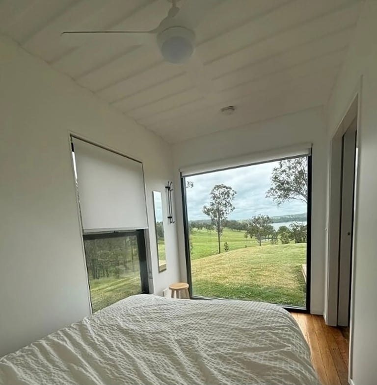 3-Bedroom Two-Story Container Home – Upper Terrace & Patio – Ground floor guest bedroom framed by a picture window and finished with warm timber flooring