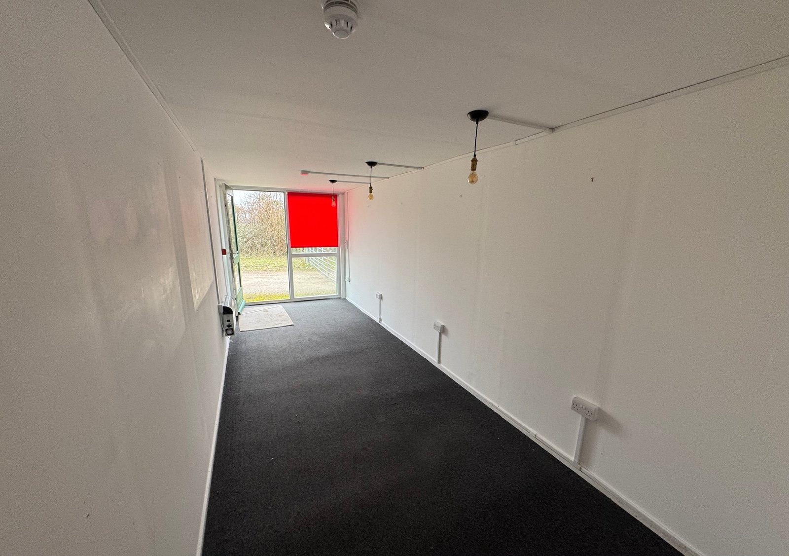 40ft Container Home – Two-Room Conversion – A spacious 40ft shipping container conversion featuring a modern white interior, dark carpeting, and large glass entry door