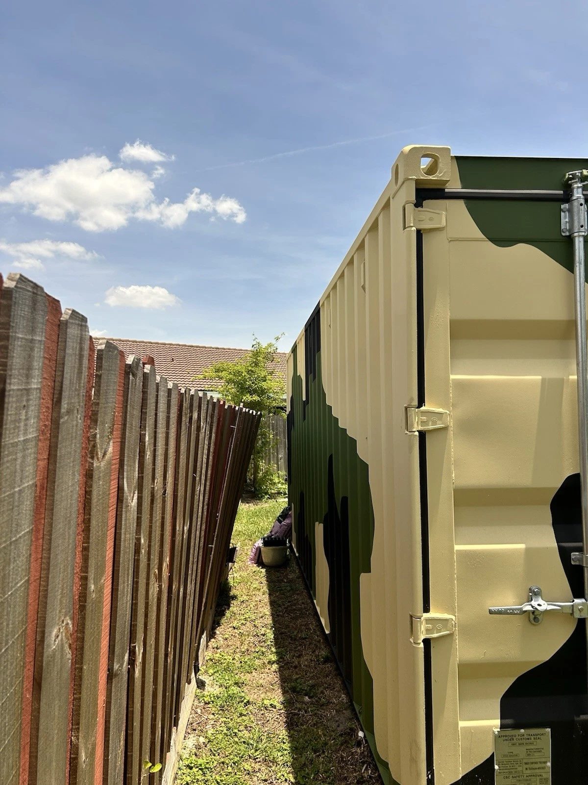 20ft Wind & Watertight Storage Container – Camouflage Finish – camouflage container side and partial closed door beside fence