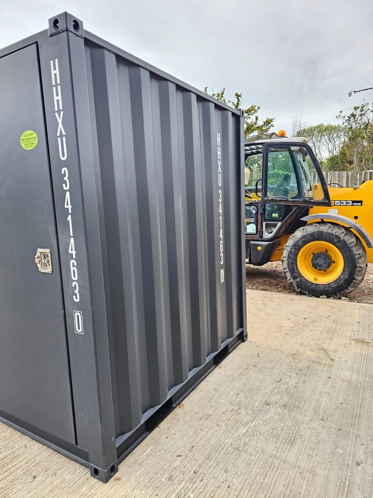 8ft New Shipping Container – Lockbox and Barred Windows – cropped grey storage container beside a yellow telehandler