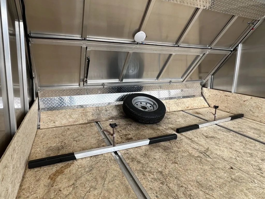 2022 High Country 12 ft Hybrid Trailer – Track Mats – Front interior section showing wood floor, tie-down bars, and a spare tire