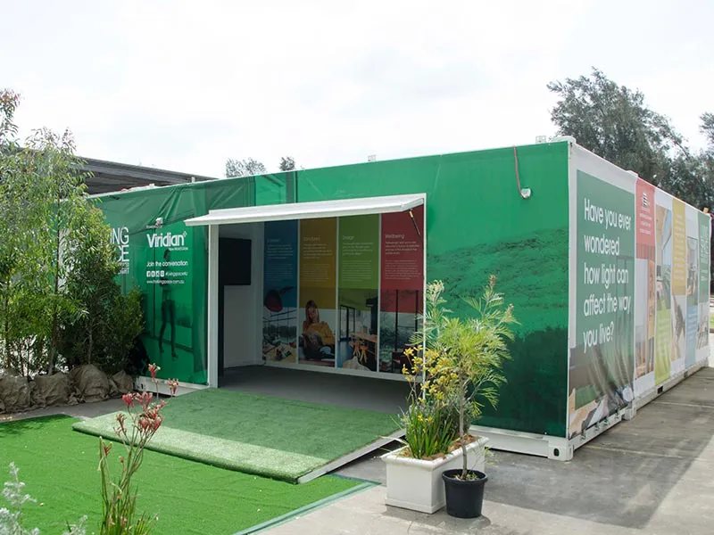 Trade Show Display Container – Lockable Steel Booth – White container unit with green graphic wraps and an open side hatch