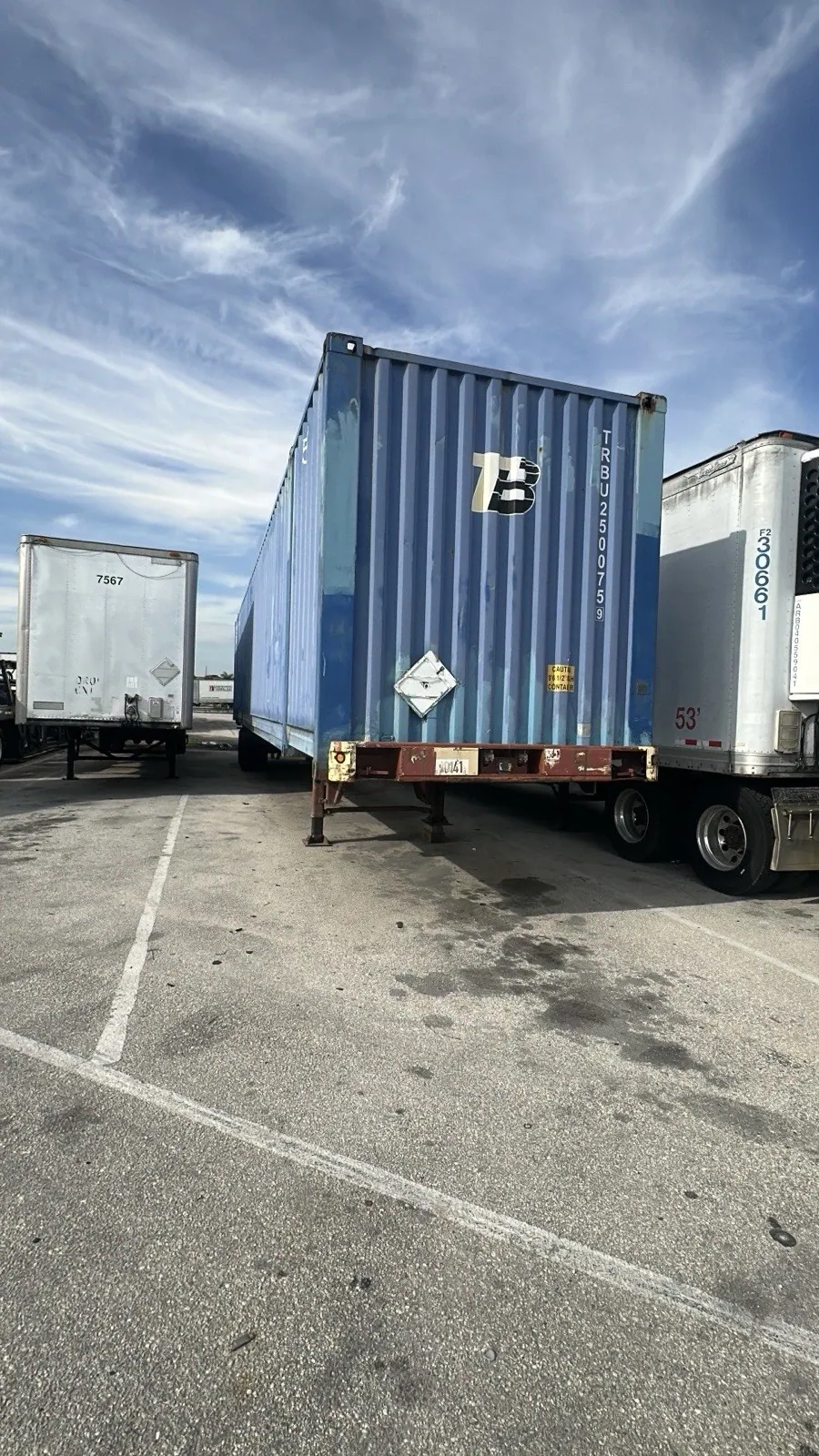 53ft High Cube Shipping Container – Used, Cargo Worthy – blue container on chassis between parked freight trailers