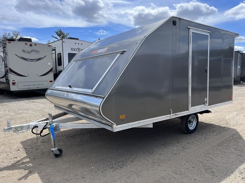 2023 Sno Pro 2-Place Snowmobile Trailer – Galvanized Package – A three-quarter exterior view of a grey snowmobile trailer with a front access hatch